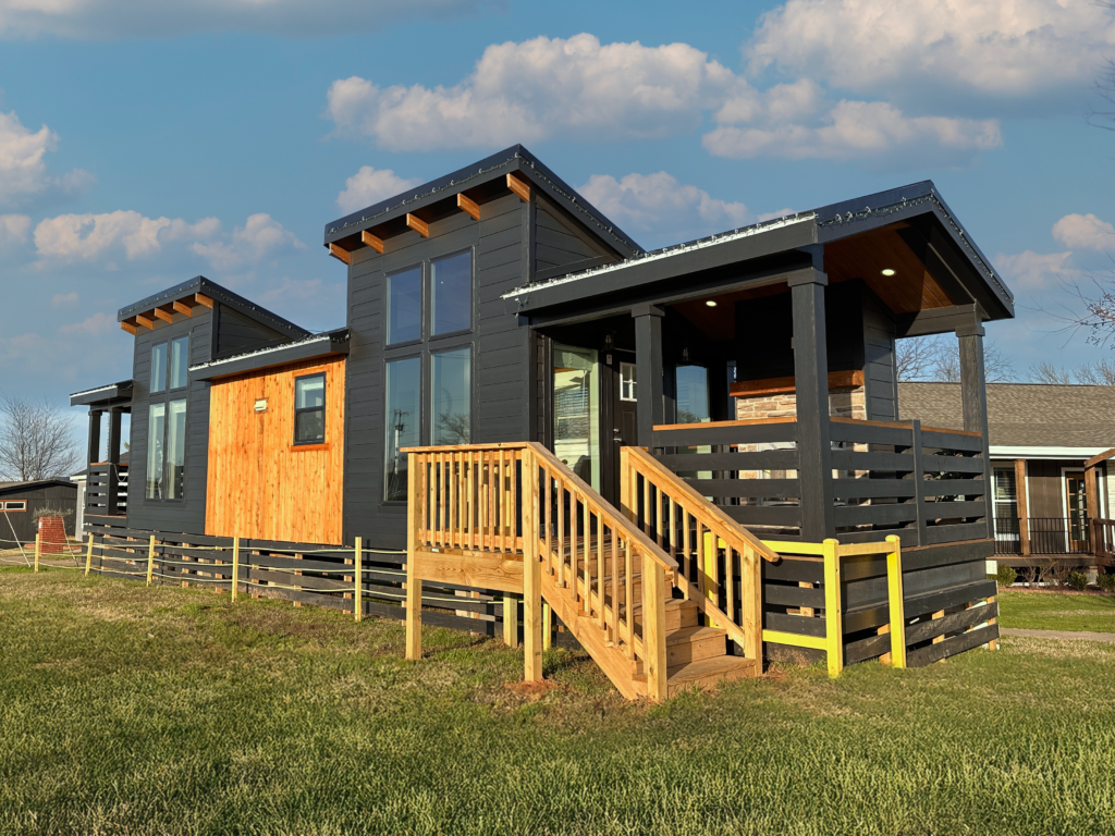 Exterior view of Pratt Homes' Round Top model, a charming tiny home with a slanted rooflines, large windows, and a cozy front & back porch, surrounded by lush greenery.